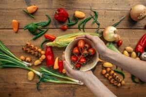 mani tengono un contenitore di pomodori e sullo sfondo un tavolo con altra verdura